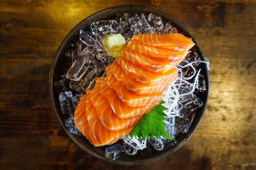 salmon shashimi - japanese raw food with wasabi on ice and sliced radish in black bowl