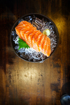 salmon shashimi - japanese raw food with wasabi on ice and sliced radish in black bowl - text space