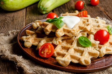vegetarian zucchini waffles with herbs on a plate with fresh tomatoes, basil and sour cream on a wooden background.