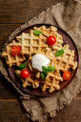 vegetarian zucchini waffles with herbs on a plate with fresh tomatoes, basil and sour cream on a wooden background.