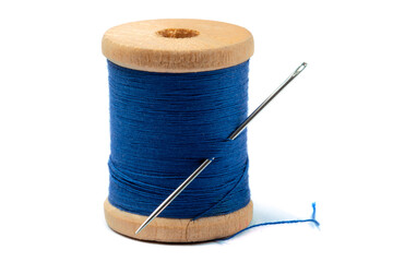 close up of blue sewing thread on a wooden spool with a sewing needle stuck in isolated on white
