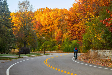 Bicyclist riding on curvy road during a beautiful autumn day with leaves turning colors