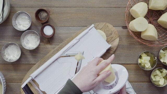 Flat lay. Slicing organic gold potatoes on a V-blade mandoline to prepare scalloped potatoes.