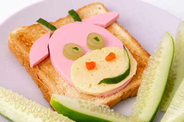 Funny sandwich with edible symbol of 2021 bull cow made from toast bread, sausage and cheese, cucumber Breakfast idea for kids. New Year Christmas food top view . holiday, celebration, food art.