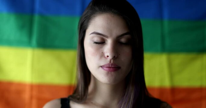 Portrait of LGBT woman standing in front of rainbow flag. Girl taking deep breath smiling at camera