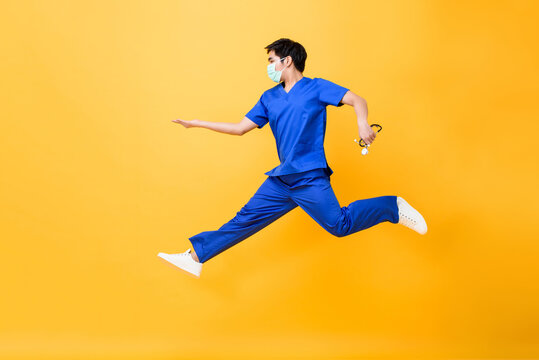 Portrait of young Asian male nurse holding stethoscope jumping in mid-air in isolated studio yellow background