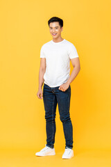Full length portrait of smiling young handsome Asian man standing with one hand in pocket isolated on yellow studio background © Atstock Productions