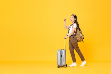 Full length travel concept portrait of beautiful smiling young Asian woman tourist with trolley bag...