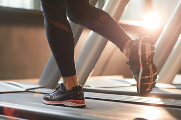 Close-up of woman in sports clothing running on treadmill in gym