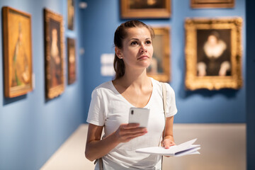 Young woman using phone for search information about painting in museum