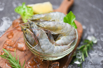 Raw shrimps prawns on ice frozen at the seafood restaurant - fresh shrimp on bowl and wooden cutting board with rosemary ingredients herb and spices for cooking seafood