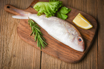 Fresh raw fish with ingredients  lemon rosemary and lettuce for making cooked food on wooden cutting board - sea bream seafood fish frozen