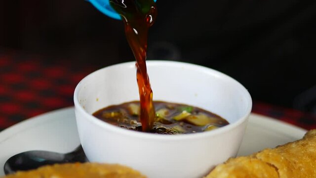 Pouring cuko (sauce of indonesian savory fish cake dish) into a white bowl. Kuah cuko is produced by adding palm sugar, chili pepper, garlic, vinegar, and salt to boiling water. 