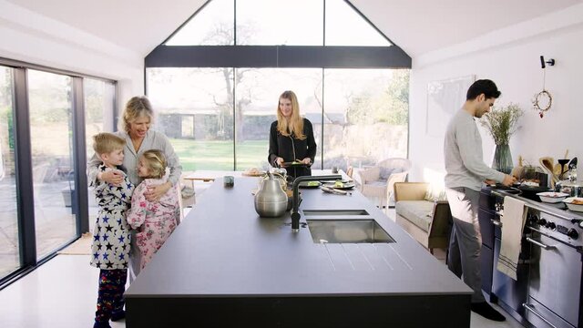 Multi-generation family in pyjamas preparing brunch at home in modern kitchen together - shot in slow motion