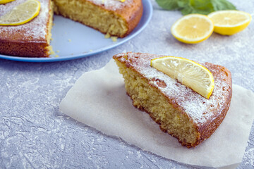 Cutting up and piece of freshly baked lemon pie, tart or semolina cake on plate served lemon wedges and mint. Homemade baking. Close up, copy space for text