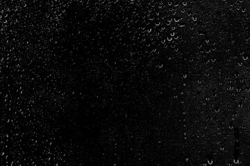 Drops of water flow down the surface of the clear glass on a black background. Texture for...