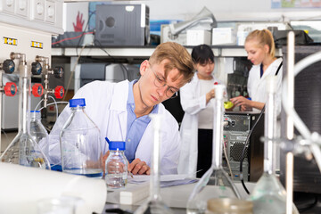 Focused student of Faculty of Biology performing experiments in university laboratory, writing results in test chart