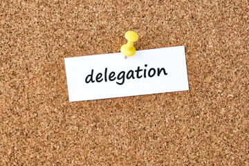 Delegation. Word written on a piece of paper, cork board background.