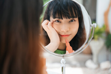 Asian young woman painting lips in pink brown colour.