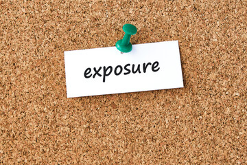 Exposure. Word written on a piece of paper, cork board background.