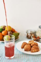 The process of pouring fruit compote in the glass, Croissants and various fruits served for breakfast on the table