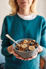 Cropped shot of woman holding homemade granola in a plate with nuts, honey, blueberries, banana and other natural ingredients, Focus on a bowl