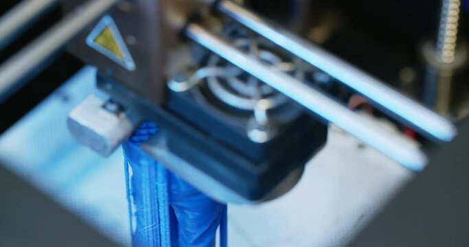 Closeup shot of a 3D printer in the process of printing a blue polymer element.