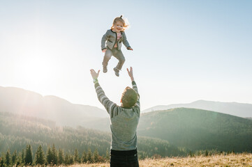 Portrait of a father holds, throws up happy daughter on hands walking on nature in autumn day. Dad...