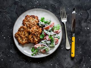 Delicious chicken breast, apple fritters and fresh tomatoes, cucumbers, arugula  yogurt dressing salad on a dark background, top view