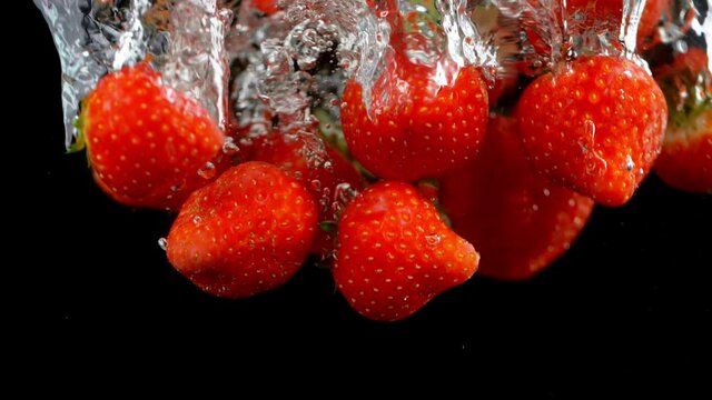 Falling strawberries into water on a black background. Filmed on high speed cinema camera, 1000fps.