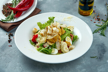 Classic caesar salad with croutons, chicken, parmesan and sauce in a white plate on a gray concrete background