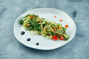 Asian style vegetarian salad with arugula, tomatoes, oranges and lettuce leaves on white plate on gray concrete background
