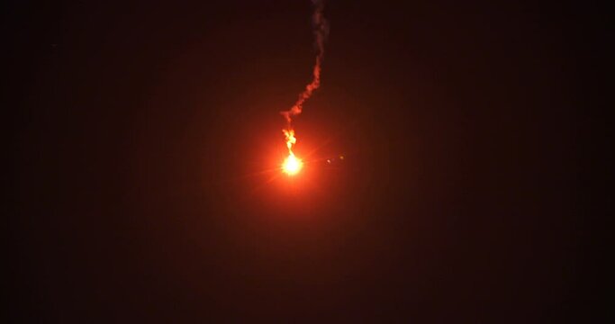 A bright red flare signal burns in the nighttime sky.