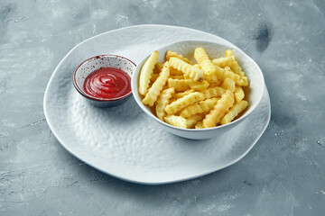 Appetizing French fries with red sauce in a white plate on a gray background