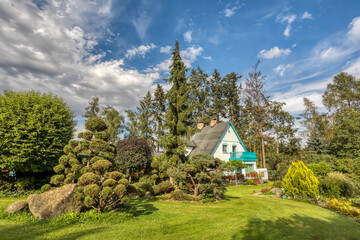 Beautiful rural house situated in late summer evergreen garden, with conifers, trees and flower. Gardening concept