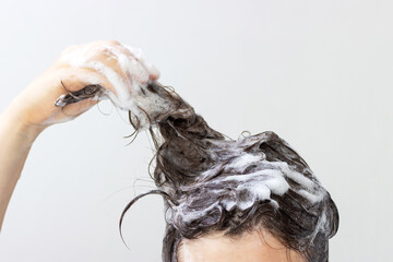 Fototapeta premium A girl washes her hair with shampoo on white background, front view