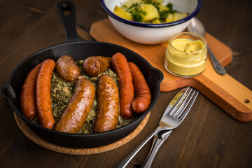 Oldenburger Grünkohl mit Pinkel, Kohlwurst, Senf und Kartoffeln in Gusseisen Pfanne auf Holz Tisch