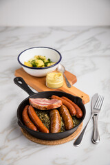 Oldenburger Grünkohl mit Pinkel, Kohlwurst, Kassler Schweine Nacken, Senf und Kartoffeln in Gusseisen Pfanne auf Marmor Tisch