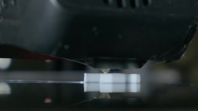 Extreme close up of 3D printer head creating white plastic detail. Futuristic technology concept. 