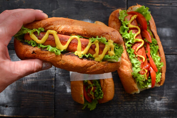 One hot-dog with mustard, ketchup, lettuce, cheese. Close up. Dark background. Woman hold a hot-dog in hands