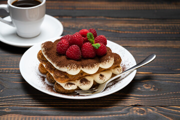 portion of Classic tiramisu dessert with raspberries and cup of espresso coffee isolated on wooden background