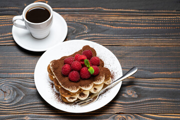 portion of Classic tiramisu dessert with raspberries and cup of espresso coffee isolated on wooden background
