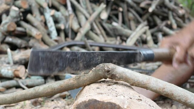 Asian senior man cutting fire wood by rusty big knife. Rural old man harvesting firewood for the winter.