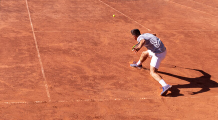 Overhead view of tennis player in action and his shadow on red clay tennis court. Young man plays tennis on the court. Sports background. Banner, copy space for text