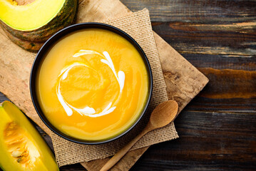 Pumpkin soup in a bowl with spoon and fresh pumpkins on wooden table, Top view