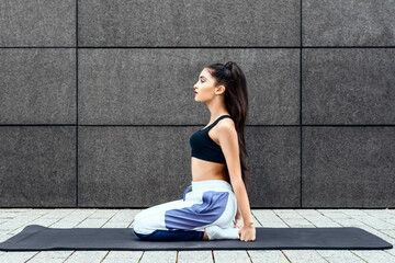 Fototapeta premium teenage girl sit on mat outdoors in urban city with sportswear and braided hair relaxing and meditating after yoga workout while concentrating on natural inner peace