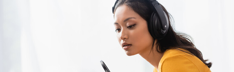 website header of pensive asian announcer in wireless headphones working in radio studio
