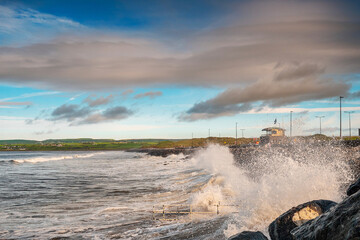 Powerful ocean wave crushes on stone shore. West coast of Ireland, Lahinch town, county Clare. Warm sunny with cloudy sky, Nobody.