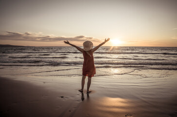 Fototapeta premium Woman in red with arms outstretched by the sea at sunrise enjoying freedom and life