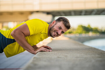 Fototapeta premium Young happy man is exercising outdoor. He is doing push-ups.